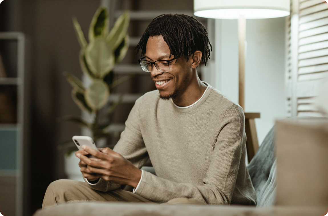 Homem negro com moletom bege mexendo no celular e sorrindo